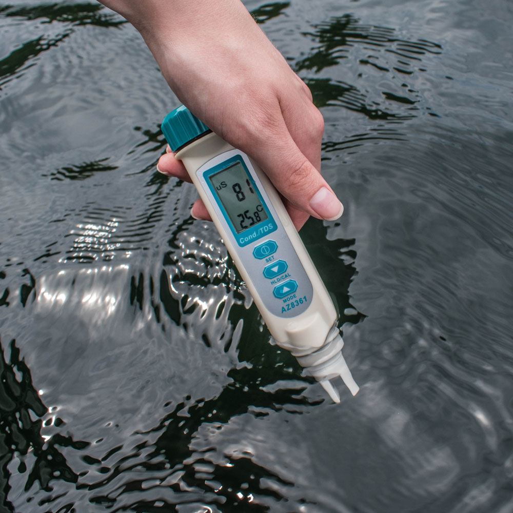 A person holding the probes of a meter in a body of water to measure conductivity.