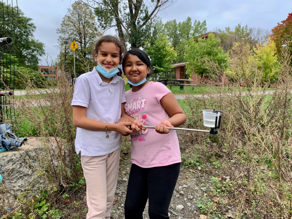 Two kids smiling and holding a reacher stick. 